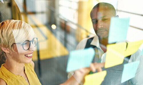 Two people working with sticky notes on wall Two people working with sticky notes on wall